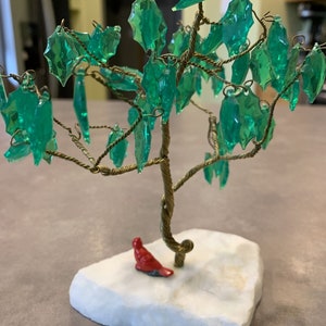 May include: A wire-wrapped tree sculpture with green glass leaves and a red cardinal figurine on a white marble base.