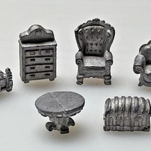 May include: Miniature silver-colored furniture set including a bed, dresser, armchair, sofa, table, and chest. The pieces have ornate details and are arranged on a white surface. The set is likely for a dollhouse or similar display.