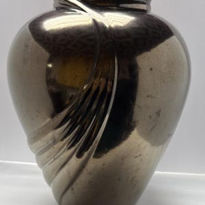 May include: A metallic silver vase with a rounded body and a narrow neck. The vase features a swirling, textured design on its surface. The vase has a reflective, polished finish, giving it a modern and elegant appearance. The vase is suitable for home decor.