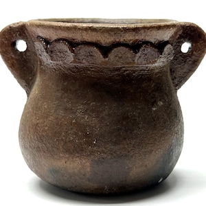 May include: A small, brown, unglazed pottery pot with two handles and a decorative rim. The pot has a rounded body and is made of a rough, textured clay.