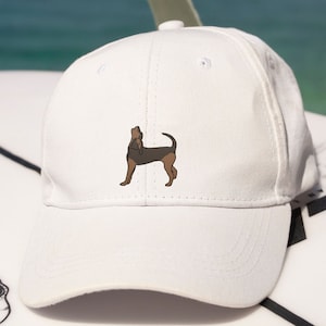 Può includere: Cappellino da baseball bianco con un'illustrazione ricamata di un cane marrone e nero.