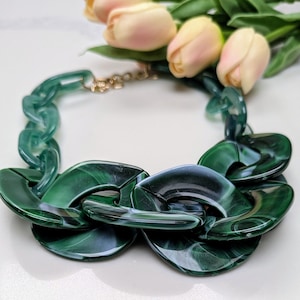 May include: A chunky green statement necklace with a chain link design. The links are large and round, with a marbled pattern.