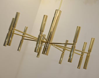 May include: A gold metal chandelier with multiple arms and cylindrical light fixtures. The chandelier has a modern design and is made of polished brass.