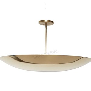 K&ouml;nnte beinhalten: Eine goldfarbene, ovale Pendelleuchte mit schlichtem, modernem Design. Die Leuchte hat eine einzelne Gl&uuml;hbirne und ein d&uuml;nnes, gerades Kabel.