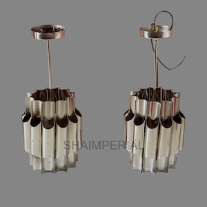 May include: Two silver pendant lights with a unique design featuring a series of vertical, fluted tubes. The lights have a simple, modern aesthetic.