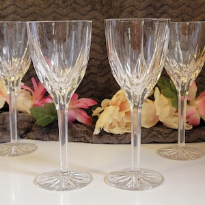 May include: A set of four clear glass wine glasses featuring a vertical cut pattern on the bowls and a starburst design on the circular bases. Each glass has a slender stem and a flared rim, showcasing a reflective, transparent finish throughout.