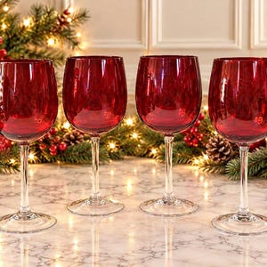 May include: A set of four wine glasses featuring deep red, translucent bowls and clear glass stems with circular bases. The glasses are arranged in a horizontal row, showcasing a smooth, polished finish and a classic, rounded silhouette.