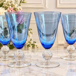 May include: A set of four blue glass goblets with clear, textured, spherical stems and circular bases. Each goblet features a deep blue bowl that tapers toward the bottom, connecting to a decorative, bumpy, clear glass ball stem.