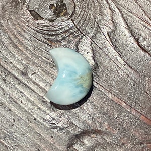 Può includere: Una pietra preziosa blu e bianca a forma di mezzaluna con un motivo verde chiaro e marrone.