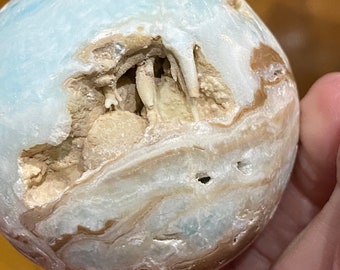 May include: A blue and brown geode sphere with a large opening revealing a cave-like interior with white crystal formations.