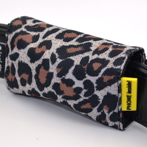 Könnte beinhalten: Ein schwarzer Ledergürtel mit einem Handy-Etui im Leopardenmuster. Das Etui hat ein gelbes Etikett mit der Aufschrift "PHONE inside".