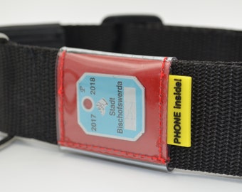 May include: Black dog collar with a red and clear plastic ID tag holder. The tag holder has a blue and white tag with the text "Stadt Bischofswerda 2017 2018". A yellow tag with the text "PHONE inside!" is attached to the collar.