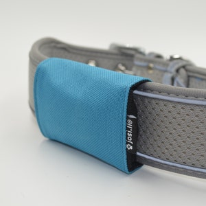 Può includere: Un collare per cani grigio con una toppa in tessuto blu che dice "josi.lilo" in testo nero. Il collare ha una striscia bianca e un design a rete.