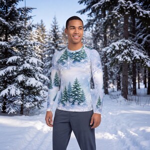 May include: A long-sleeve crew neck shirt featuring a winter landscape print with green pine trees, white snowflakes, and swirling white patterns against a light blue background, paired with solid dark gray pants.