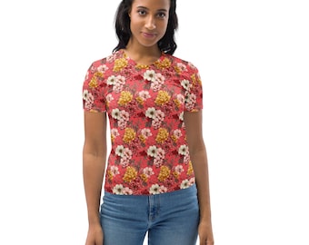 May include: A short-sleeved V-neck shirt with a vibrant floral pattern. The shirt features a red background with a repeating design of yellow, white, and pink flowers. The model is wearing blue jeans.