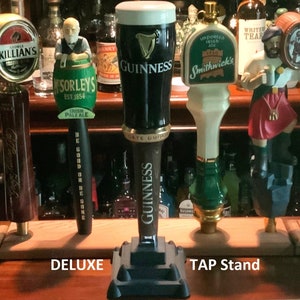 Puede incluir: Un soporte de grifo de madera con cuatro grifos de cerveza. Los grifos est&aacute;n decorados con varios dise&ntilde;os, incluyendo un grifo verde y dorado con el texto "Sorleys Est 1854 Irish Pale Ale", un grifo negro y dorado con el texto "Guinness", un grifo blanco y verde con el texto "Smithwick's", y un grifo marr&oacute;n y dorado con la figura de un hombre con una falda escocesa roja.