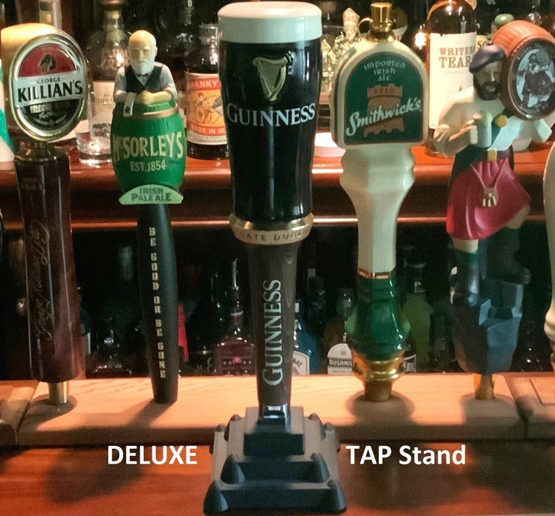 Puede incluir: Un soporte de grifo de madera con cuatro grifos de cerveza. Los grifos est&aacute;n decorados con varios dise&ntilde;os, incluyendo un grifo verde y dorado con el texto "Sorleys Est 1854 Irish Pale Ale", un grifo negro y dorado con el texto "Guinness", un grifo blanco y verde con el texto "Smithwick's", y un grifo marr&oacute;n y dorado con la figura de un hombre con una falda escocesa roja.