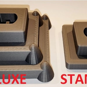 Puede incluir: Dos soportes de exhibici&oacute;n impresos en 3D para figuras o modelos. El soporte de la izquierda est&aacute; etiquetado como "DELUXE" y tiene tres niveles. El soporte de la derecha est&aacute; etiquetado como "STANDARD" y tiene dos niveles.