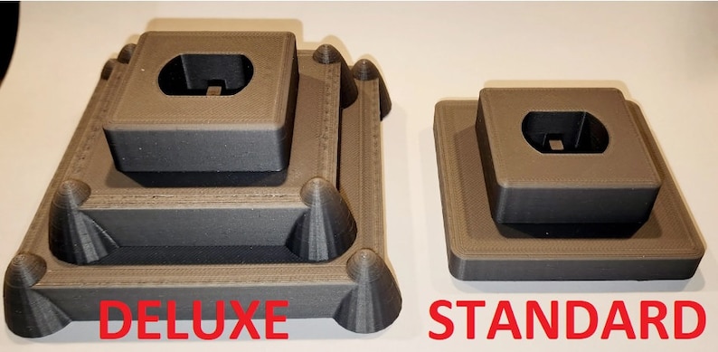 Puede incluir: Dos soportes de exhibici&oacute;n impresos en 3D para figuras o modelos. El soporte de la izquierda est&aacute; etiquetado como "DELUXE" y tiene tres niveles. El soporte de la derecha est&aacute; etiquetado como "STANDARD" y tiene dos niveles.