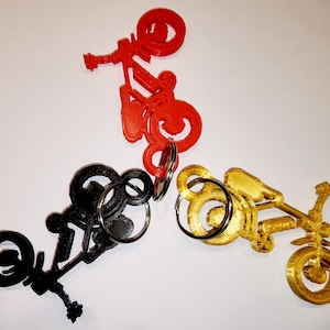 May include: Three 3D-printed bicycle keychains in red, black, and gold. Each keychain features a detailed bicycle design with a key ring attached. The keychains are arranged in a triangular pattern against a white background.