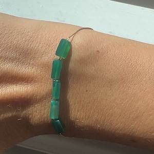 Op de afbeelding: Een armband van groene edelstenen met rechthoekige kralen op een dunne gouden ketting.