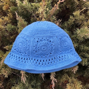 May include: A blue crocheted bucket hat with a circular pattern. The hat is made with a soft yarn and has a wide brim.