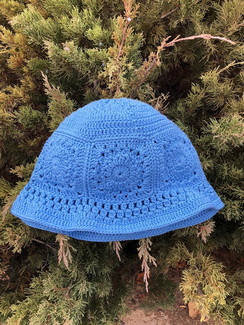 May include: A blue crocheted bucket hat with a circular pattern. The hat is made with a soft yarn and has a wide brim.