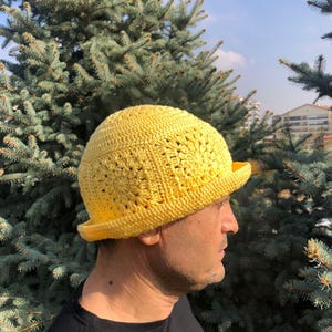 May include: A yellow crocheted hat with a wide brim. The hat is made with a square stitch pattern.