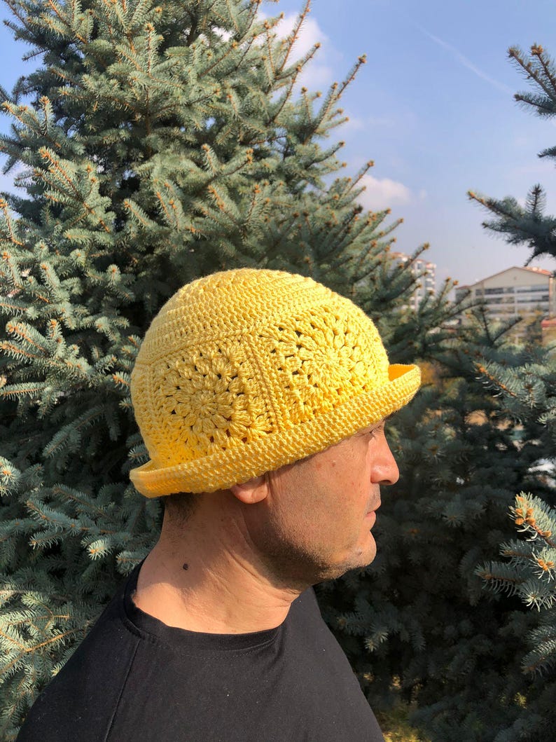 May include: A yellow crocheted hat with a wide brim. The hat is made with a square stitch pattern.