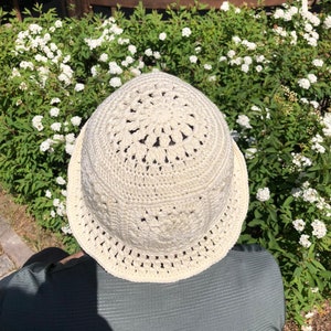 May include: A white crocheted bucket hat with a detailed design. The hat is made with a delicate openwork pattern.