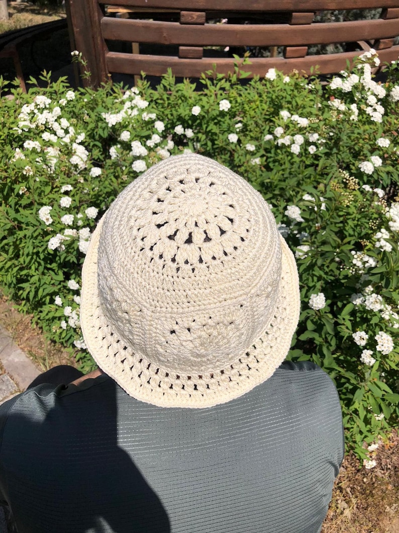 May include: A white crocheted bucket hat with a detailed design. The hat is made with a delicate openwork pattern.
