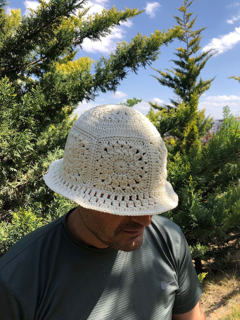 May include: A white crocheted bucket hat with a lacy design. The hat is worn by a person with a beard and a green shirt.