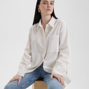 A woman sitting on a wooden block wearing a Women White Linen Oversized Shirt and jeans.