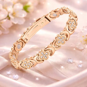 May include: A gold-colored bracelet with a floral design. The bracelet features a series of flower-shaped links, each adorned with small, sparkling crystals. The clasp is a simple, secure design. The background is a soft, blurred image of flowers.