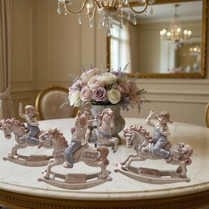 May include: Three porcelain figurines of children riding rocking horses. Each figurine features a child in blue overalls sitting on a white horse with pink accents. The horses have curved rockers and the children are depicted in various poses.
