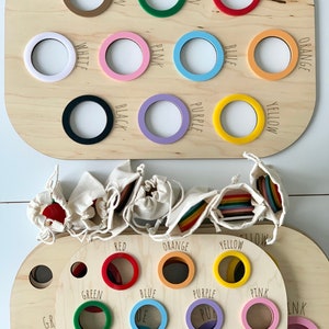 Peut inclure: Jouet en bois avec deux plateaux circulaires. Le plateau supérieur comporte 12 anneaux de couleur avec le nom de la couleur écrit sous chaque anneau. Le plateau inférieur comporte 12 trous avec le nom de la couleur écrit sous chaque trou. Les anneaux sont dans des sacs aux couleurs de l'arc-en-ciel.