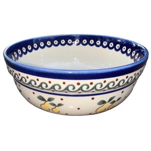 May include: A round ceramic bowl with a cream-colored base featuring a hand-painted pattern of yellow pears with green leaves, brown dots, and a blue wavy line border. The rim is decorated with a blue band containing white circles.