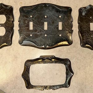 May include: Set of five antique-style electrical wall plates. The plates are bronze-colored with a textured surface and decorative edges. Includes plates for a double outlet, three switches, a single switch, and a blank plate.
