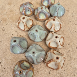 May include: A collection of 12 ceramic beads in various shades of green, white, and brown. The beads are irregularly shaped and have a textured surface. Each bead has a small hole in the center.
