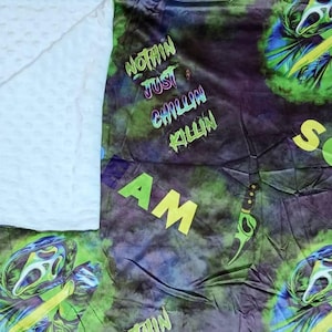 May include: A Scream-themed blanket with a white, textured backing. The patterned side features the Ghostface killer in green and blue, with the words "SCREAM", "NOTHIN JUST CHILLIN KILLIN", and "AM".