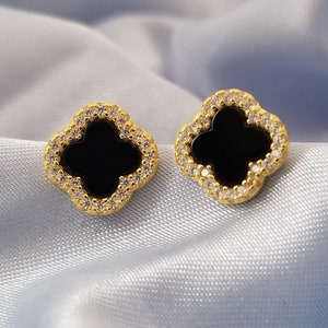 May include: A pair of gold-tone earrings with a black clover-shaped design and clear cubic zirconia stones.