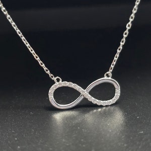 May include: A silver infinity necklace with small clear cubic zirconia stones set around the infinity symbol.