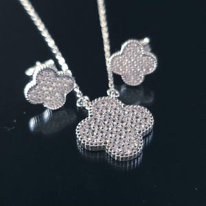May include: A silver necklace and earrings set with a four-leaf clover pendant and matching earrings. The clover is covered in small, clear stones.