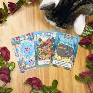 May include: Three fantasy-themed cards with illustrations and text. The cards are labeled "COPY", "FOOD", and "TREASURE". The "FOOD" card depicts a bowl of fruit. The "TREASURE" card shows a treasure chest. A cat is partially visible.