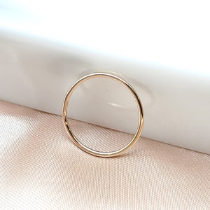 Könnte beinhalten: Ein zarter, dünner Goldring. Der Ring ist ein schlichtes Band mit polierter Oberfläche, das Licht reflektiert. Der Ring ist vor einem weichen, neutralen Hintergrund platziert, der sein minimalistisches Design hervorhebt. Ein Schmuckstück.