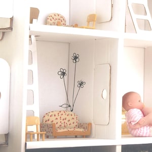 May include: A white dollhouse with a red and white floral patterned couch, a ladder, and a small chair. The dollhouse has a white wall with a black flower design.