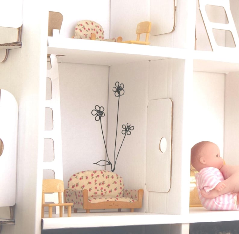 May include: A white dollhouse with a red and white floral patterned couch, a ladder, and a small chair. The dollhouse has a white wall with a black flower design.