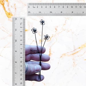 May include: A black wire sculpture of three flowers with five petals each. The sculpture is about 7.5 inches tall and is held in a person's hand for scale.