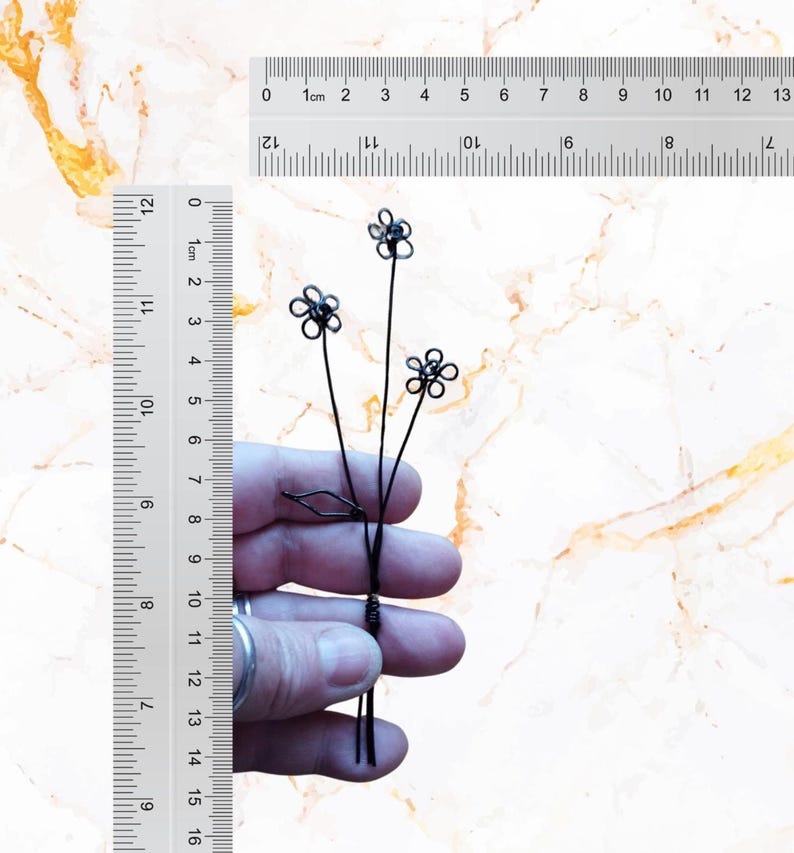 May include: A black wire sculpture of three flowers with five petals each. The sculpture is about 7.5 inches tall and is held in a person's hand for scale.