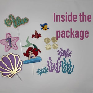 May include: A set of mermaid-themed cake toppers, including a purple seashell, a starfish with the number 7, a mermaid with red hair, a blue fish, a red crab, and various seaweeds. The text "Alice" and "Inside the package" are also included.